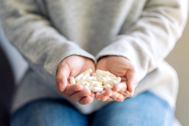 Closeup image of a woman holding white medicine capsules in hand