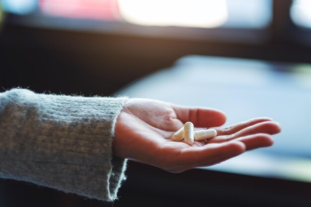 Closeup image of a woman holding white medicine capsules in hand