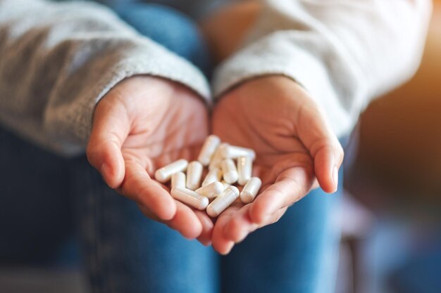 Closeup image of a woman holding white medicine capsules in hands