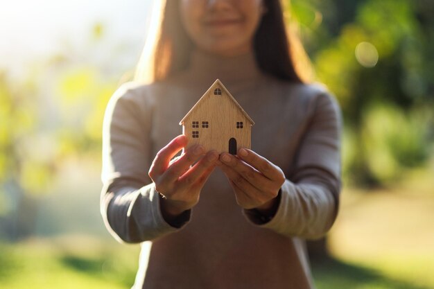 Foto immagine del primo piano di una donna che tiene il modello di casa in legno in mezzo alla natura