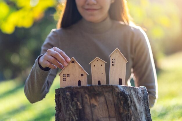 Closeup image of a woman holding wooden house models on tree stump in the outdoors