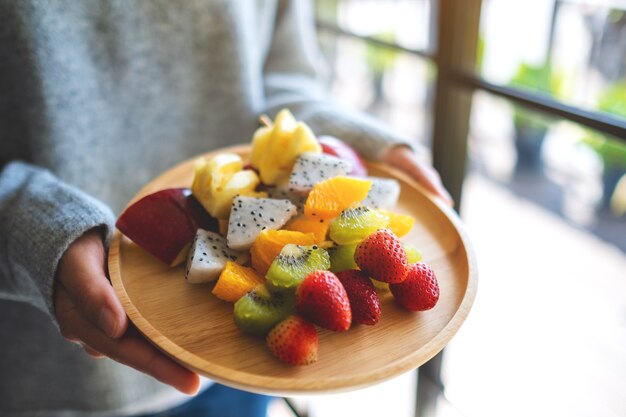 Closeup image of a woman holding a wooden plate of fresh mixed fruits on skewers