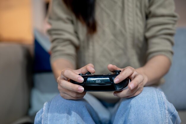 家のソファでジョイスティックを握ってビデオゲームをしている女性のクローズアップ画像