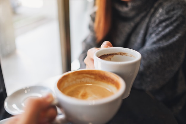 Closeup image of a woman and a man clinking coffee mugs in cafe