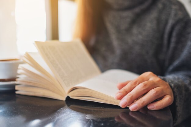 Closeup image of a woman opening and reading a vintage novel book on the table