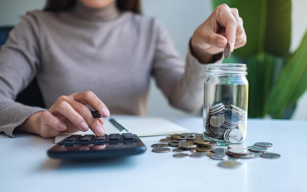 Closeup image of a woman putting coins in a glass jar  calculating and taking note for saving money and financial concept