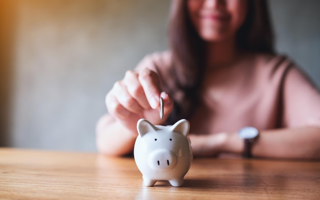 Closeup image of a woman putting coins into piggy bank for saving money concept