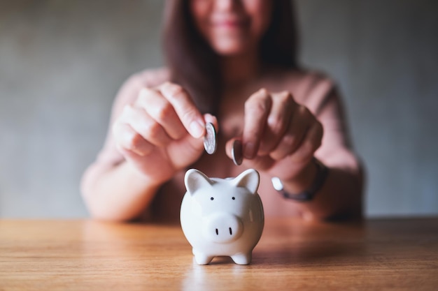 Closeup image of a woman putting coins into piggy bank for saving money concept