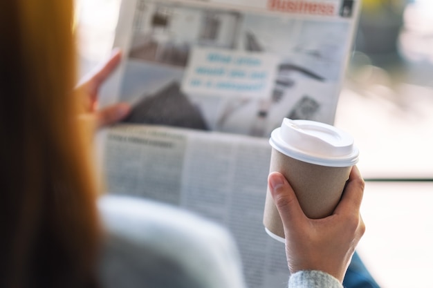 Closeup image of a woman reading newspaper and drinking coffee in the morning