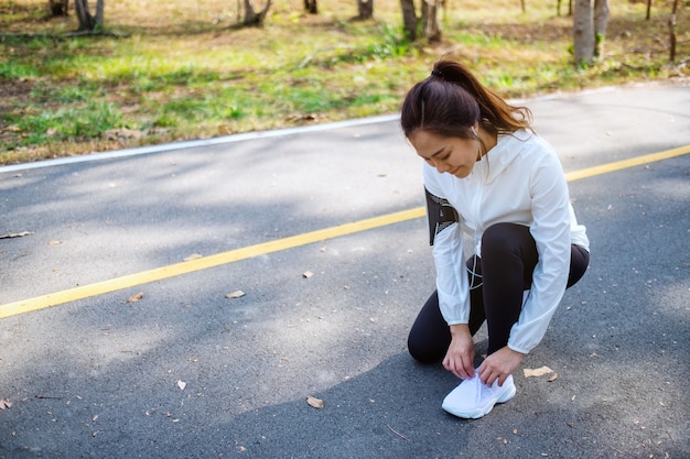 靴ひもを結び、都市公園で実行の準備をしている女性ランナーのクローズアップ画像