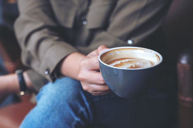 Closeup image of a woman's hand holding and drinking hot latte coffee while sitting in cafe