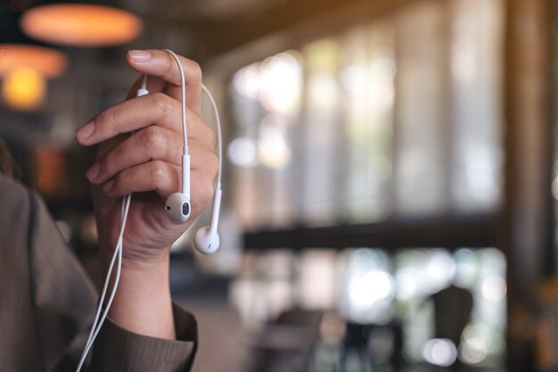 カフェで音楽を聴くためにイヤホンを持っている女性の手のクローズアップ画像