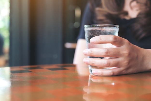 テーブルに冷たい水のガラスを持っている女性の手の拡大画像