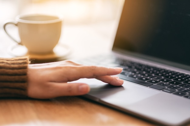 Closeup image of a woman's hand using and touching on laptop touchpad on wooden table