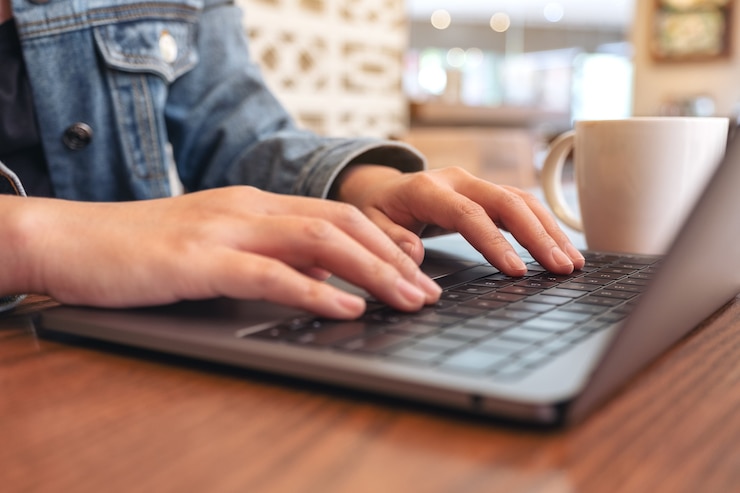 Photo closeup image of woman's hands using and typing on laptop computer keyboard with coffee cup on the table