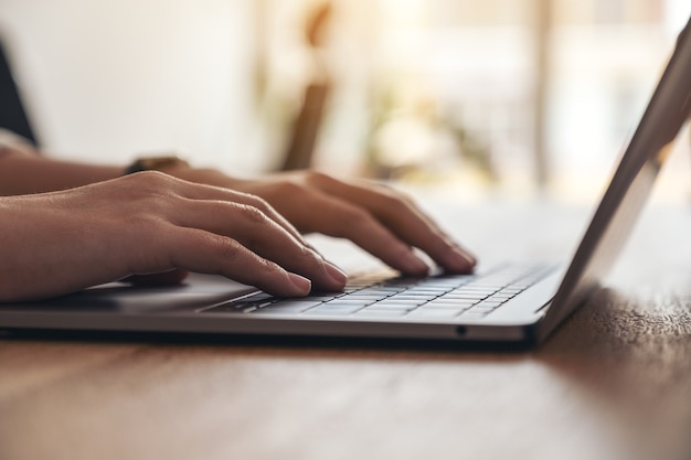 Closeup image of woman's hands using and typing on laptop keyboard on the table