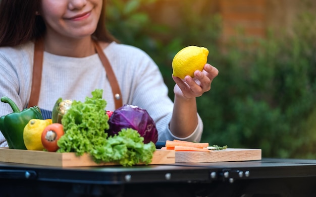 Closeup image of a woman selecting lemon from a mixed vegetables in wooden tray