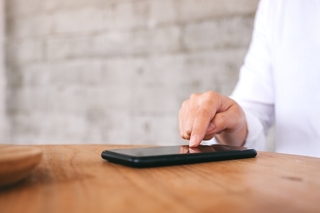 Closeup image of a woman touching and pointing at mobile phone screen on wooden table