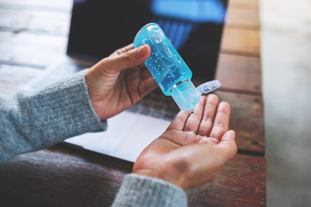 Closeup image of a woman using and applying alcohol gel to clean hands while working on laptop at home for Healthcare and Covid-19 or 2020 virus concept