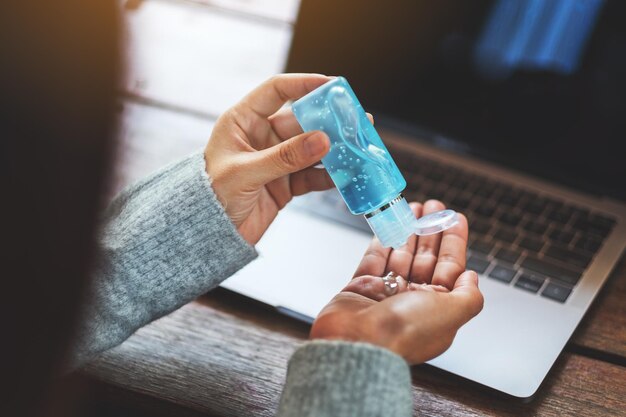 Closeup image of a woman using and applying alcohol gel to clean hands while working on laptop at home for Healthcare and Covid-19 concept