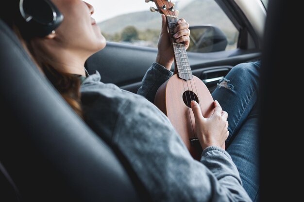 Closeup image of a woman with headphone playing Ukulele while riding in the car