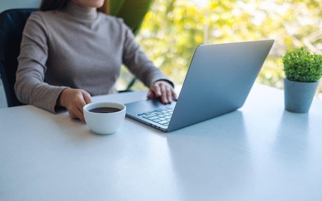 Крупным планом изображение женщины, работающей и касающейся сенсорной панели ноутбука во время питья кофе