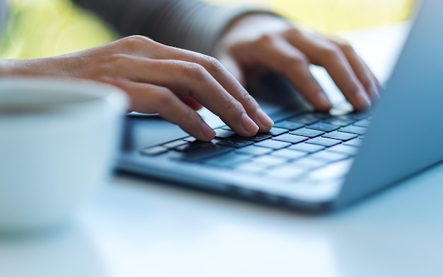 Closeup image of a woman working and typing on laptop computer keyboard on the table