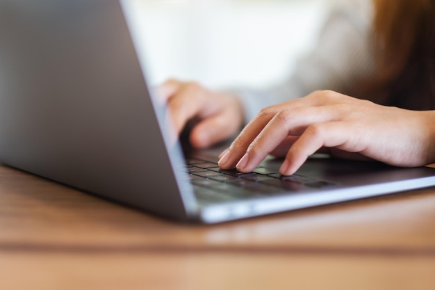 Closeup image of a woman working and typing on laptop computer keyboard on wooden table