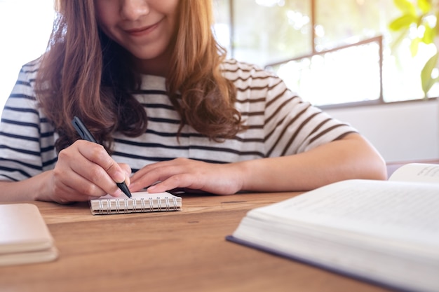 Photo closeup image of a woman writing on blank notebook and books on wooden table while learning