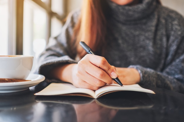 Closeup image of a woman writing on a blank notebook on the table