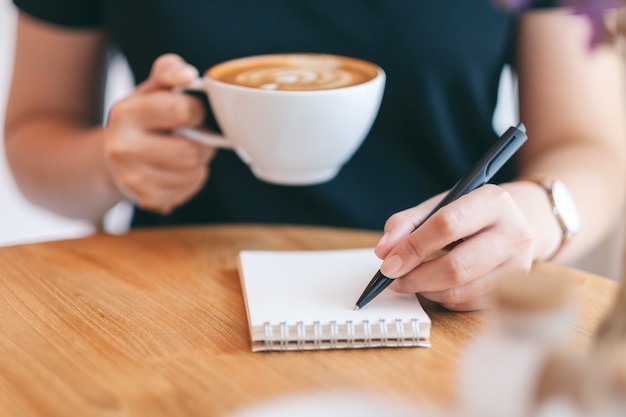 Foto immagine del primo piano di una donna che scrive su un taccuino bianco mentre beve caffè