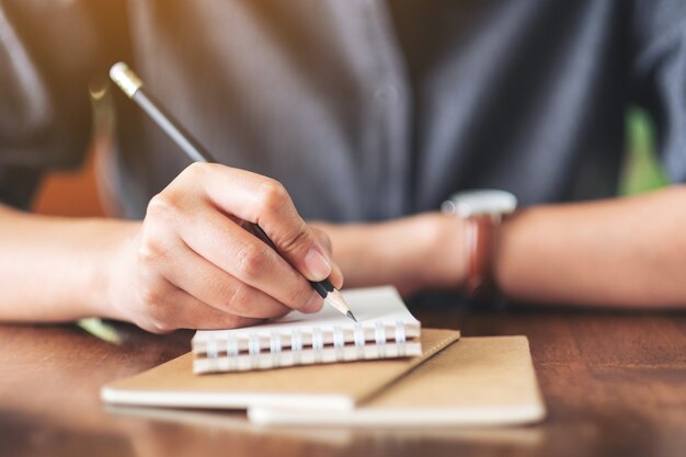 Closeup image of a woman writing on blank notebook with coffee cup on table in cafe