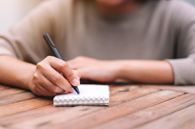 Closeup image of a woman writing on blank notebook on wooden table