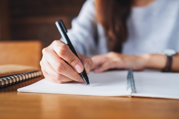 Крупным планом изображение женщины, пишущей на пустой записной книжке на деревянном столе