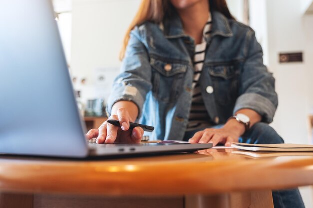 Closeup image of a woman writing on a notebook while working on laptop computer in office