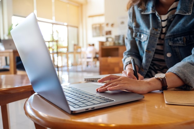 Foto immagine del primo piano di una donna che scrive su un taccuino mentre lavora al computer portatile in ufficio