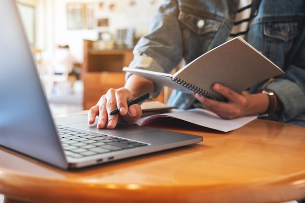 Closeup image of a woman writing on a notebook with laptop computer on the table