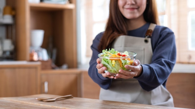 自宅のキッチンで新鮮な混合野菜のサラダを持って見せている若いアジアの女性のクローズアップ画像