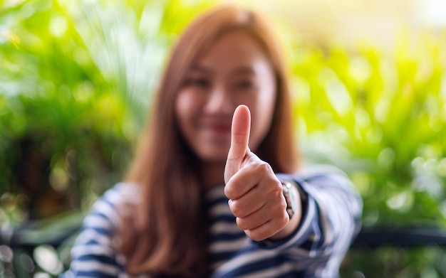 Photo closeup image of a young asian woman making and showing thumbs up hand sign