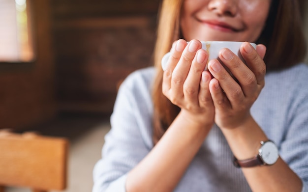 Closeup image of a young asian woman smelling and drinking hot coffee