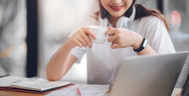 Immagine del primo piano del caffè bevente della giovane donna attraente mentre lavorando con il computer portatile a casa.