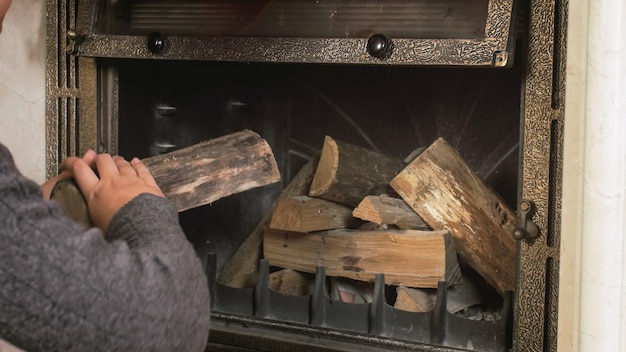 Photo closeup image of young man throwing wood in fireplace