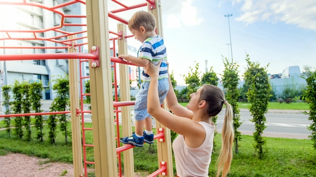 스포츠 어린이 놀이터에서 높은 금속 계단에 등반 그녀의 작은 아들을 돕는 젊은 어머니의 근접 촬영 이미지