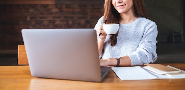 Immagine del primo piano di una giovane donna che beve caffè mentre lavora al computer portatile