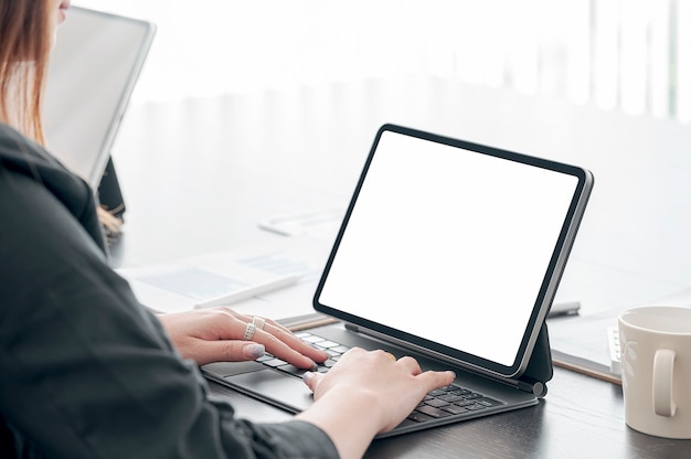 Closeup image of young woman hand working on tablet keyboard while sitting at office desk