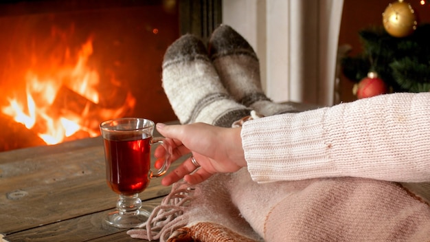 Closeup image of young woman holding cup of tea at burning fireplace