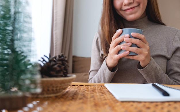 Closeup image of a young woman holding and drinking coffee while study at home