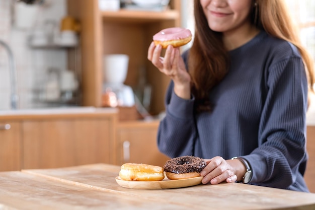 Immagine del primo piano di una giovane donna che tiene e si diverte a mangiare le ciambelle a casa