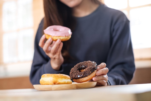 Photo closeup image of a young woman holding and enjoyed eating donuts at home