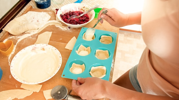 Closeup image of young woman making cupcakes. Girl putting creme inside of the dough in silicone forms for baking